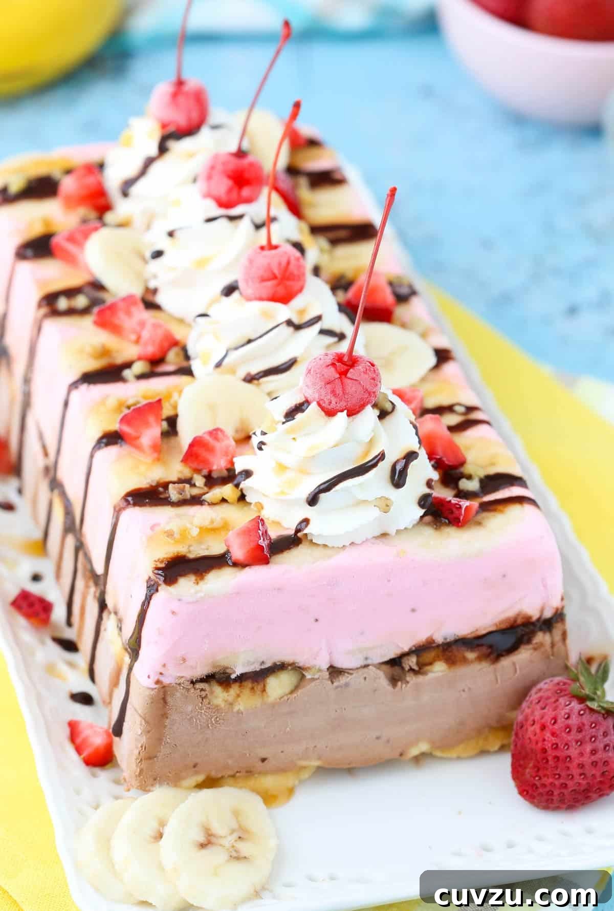 Frozen Banana Split Loaf 2 A beautifully layered banana split ice cream cake loaf on a pristine white tray, showcasing its vibrant colors and inviting texture. The cake is perfectly shaped, ready to be sliced and enjoyed.