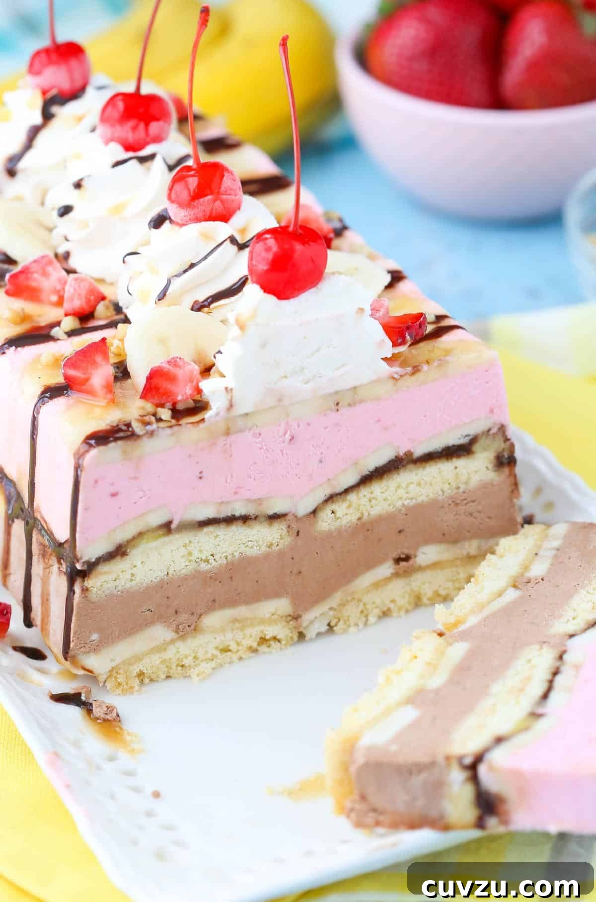 Frozen Banana Split Loaf 3 A close-up view of a sliced banana split ice cream cake loaf, revealing the distinct layers of strawberry and chocolate ice cream, fresh bananas, and shortbread, all resting on a white tray.