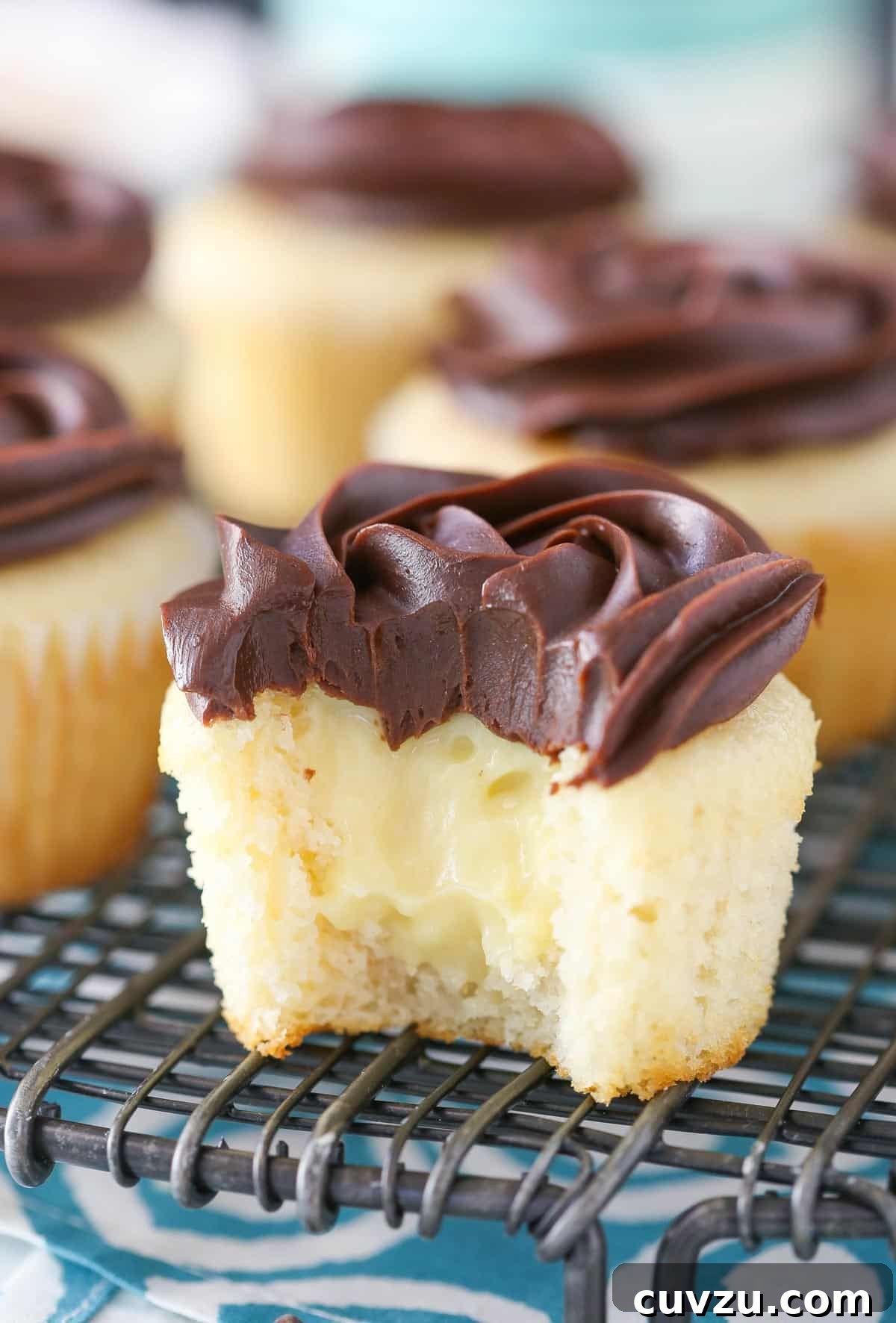 Decadent Boston Cream Cupcakes 3 A Boston cream pie cupcake with a bite taken out, revealing the creamy vanilla pastry filling.