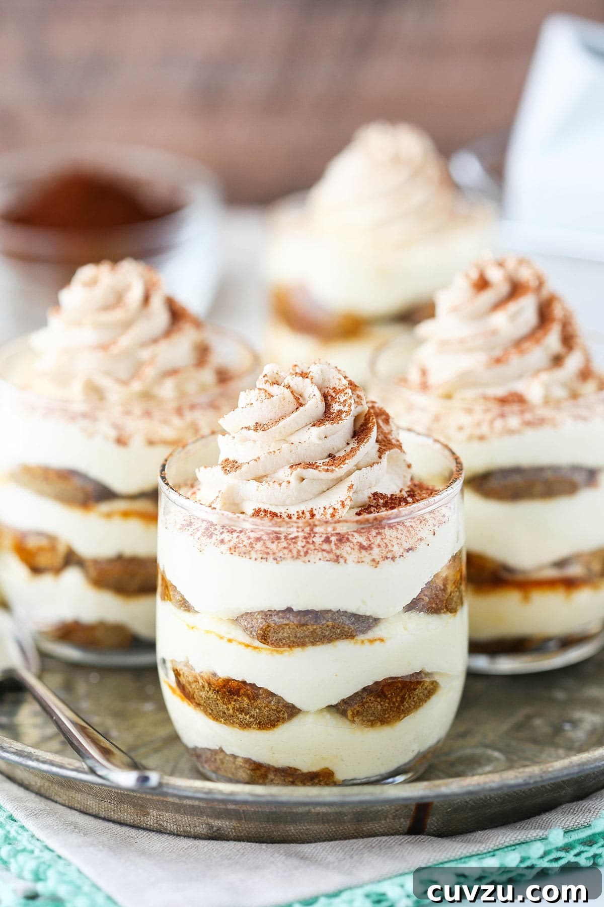 Tiramisu Bites 3 A metal tray holding three tiramisu trifles with another trifle and a dish full of cocoa powder behind the tray
