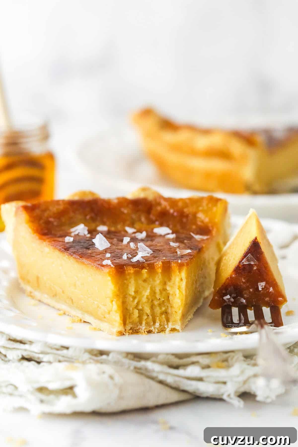 Perfectly salty and sweet, this Salted Honey Pie features a creamy custard-based filling in a classic butter pie crust. A slice of salted honey pie on a plate, with a bite on a fork