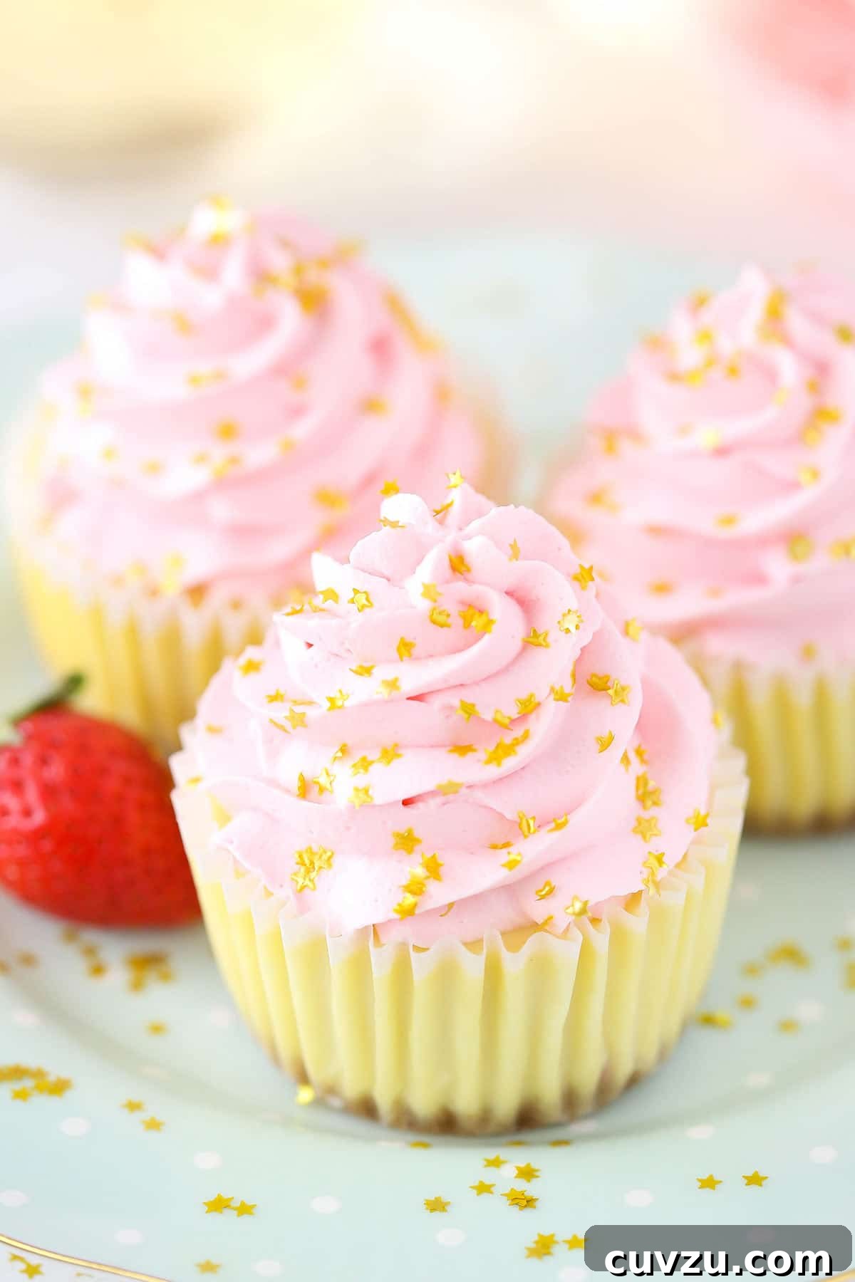 Bubbly Strawberry Cheesecake Bites 6 A close-up of three beautifully crafted strawberry champagne cheesecake cupcakes arranged on a charming polka-dotted plate, highlighting their individual elegance and inviting texture.
