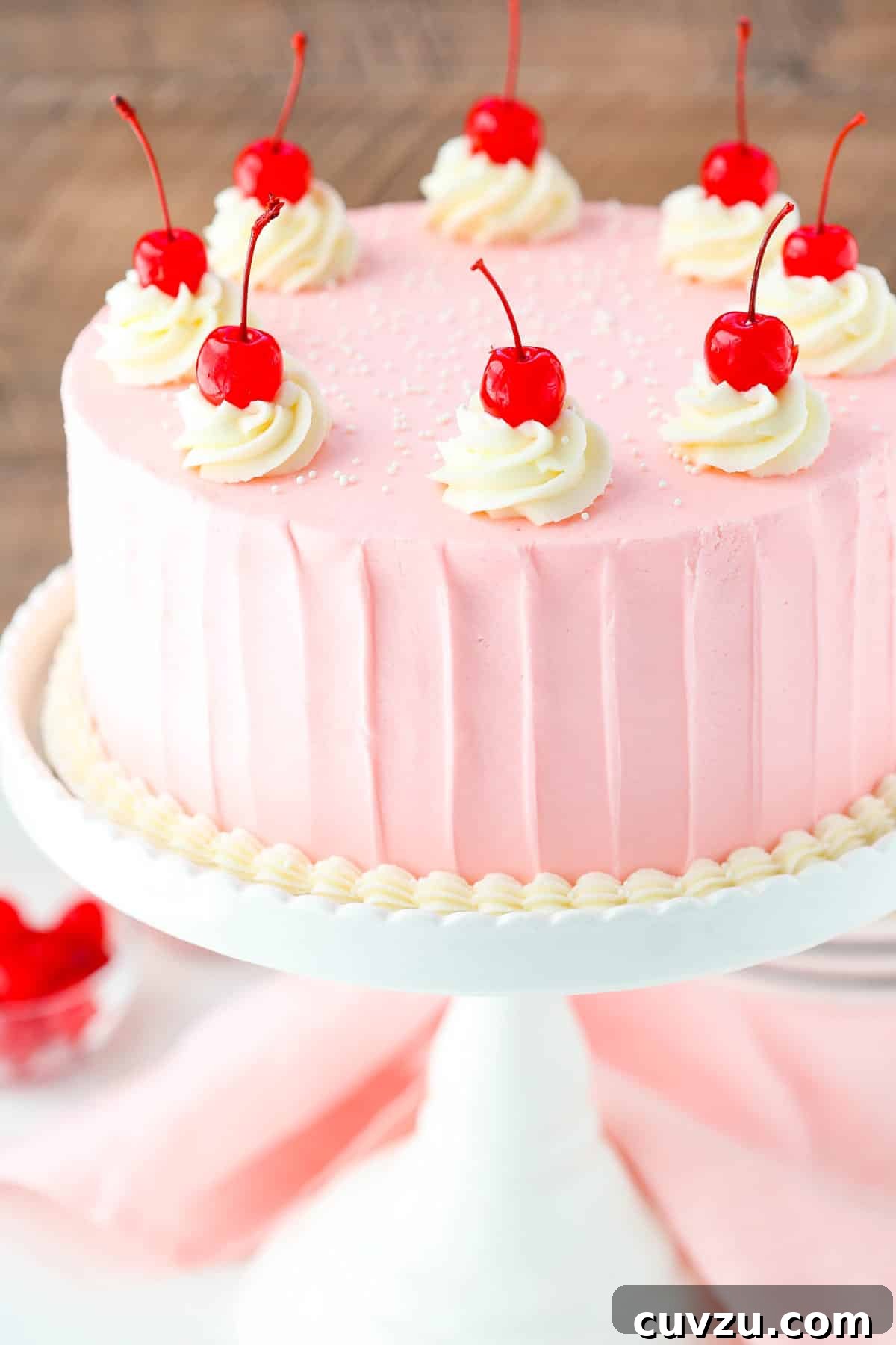 Decadent Cherry Almond Dream Cake 2 Top view of a cherry almond layer cake on a white cake stand, showcasing its beautiful frosting and cherry decorations.