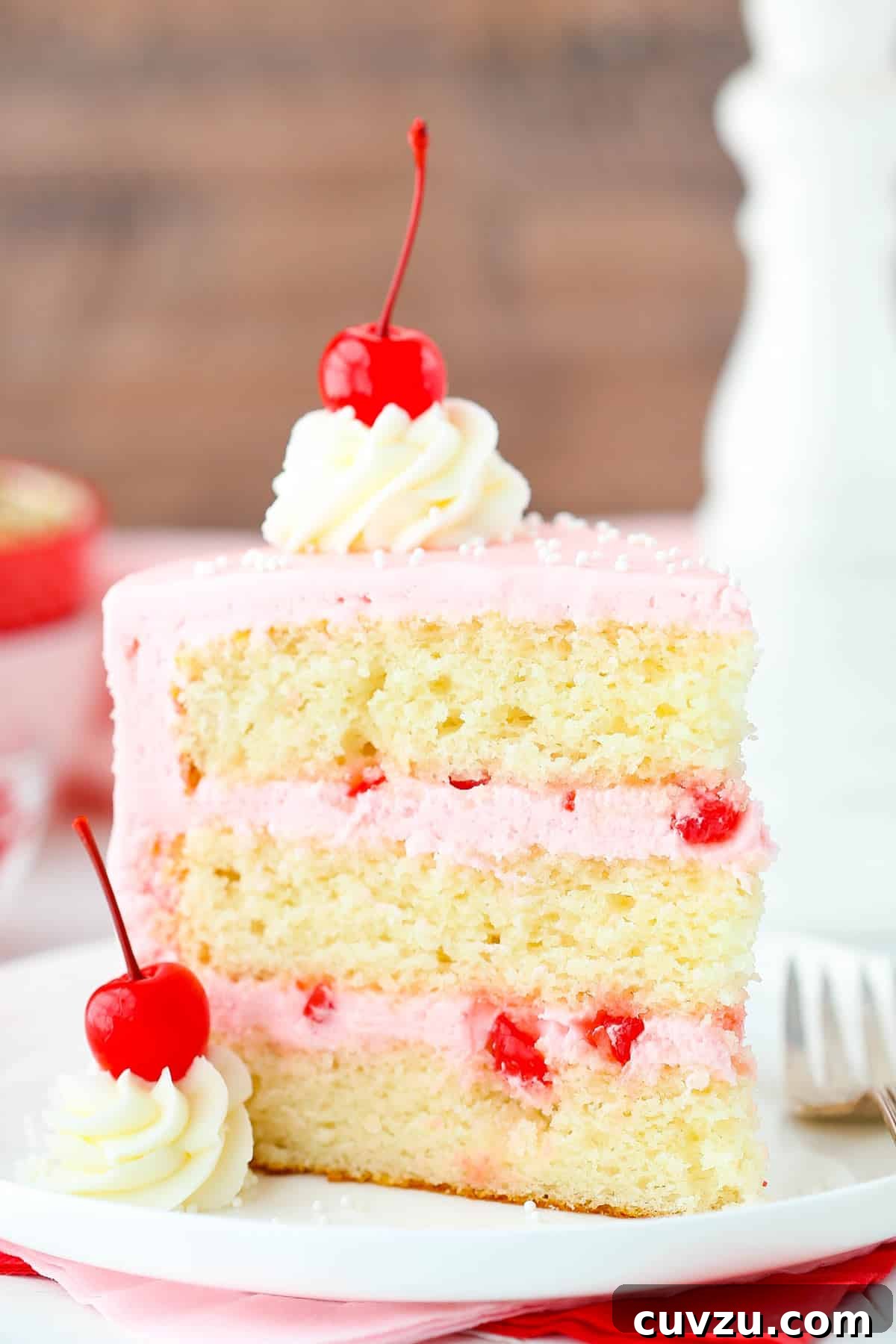 Decadent Cherry Almond Dream Cake 4 A slice of cherry almond layer cake on a white cake plate, showing the texture of the cake and the thick layers of frosting.