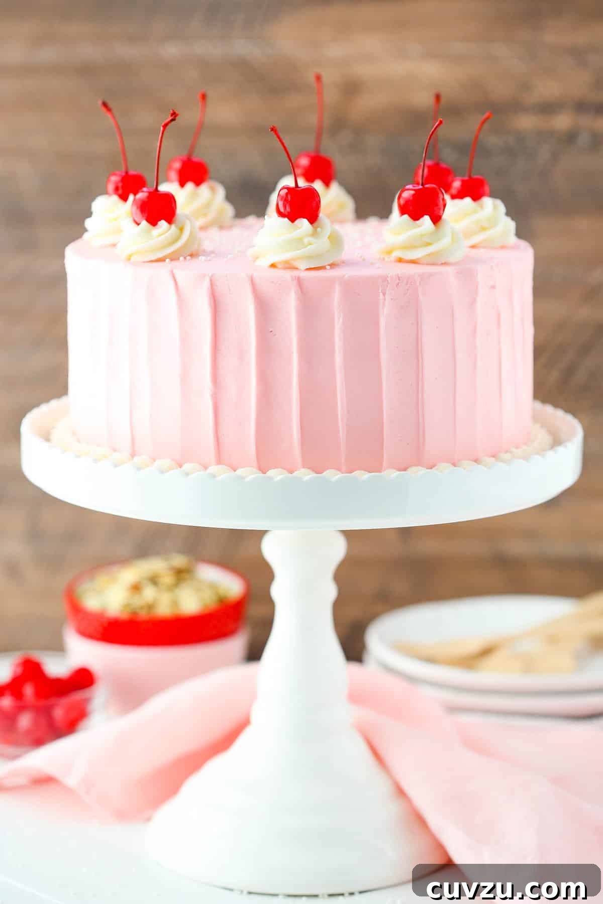 Decadent Cherry Almond Dream Cake 5 A full cherry almond layer cake on a white cake stand, showcasing the striped frosting and cherry decorations.