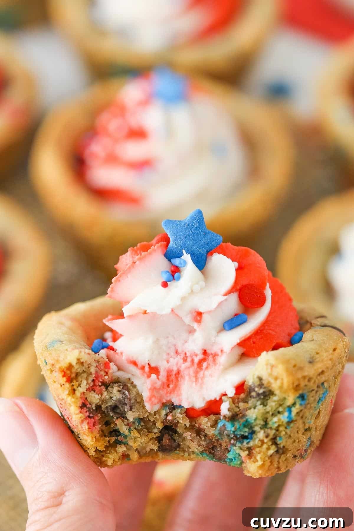 Stars and Stripes Chocolate Chip Cookie Cups 5 A hand holding up a single patriotic chocolate chip cookie cup with a bite missing, highlighting its soft texture and colorful frosting.