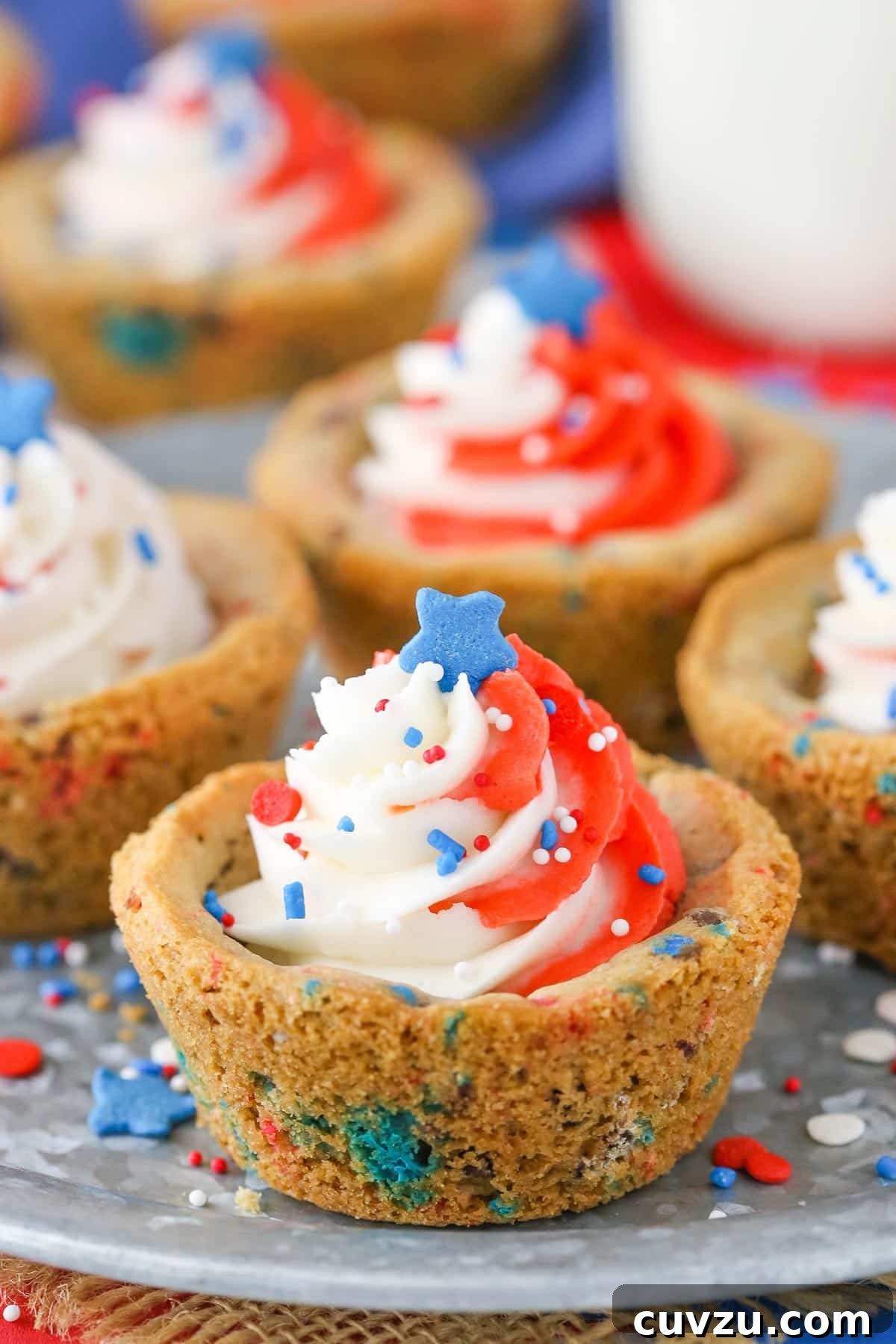 Stars and Stripes Chocolate Chip Cookie Cups 6 Close-up of a single patriotic chocolate chip cookie cup, showcasing the intricate swirl of red and white frosting and scattered sprinkles.
