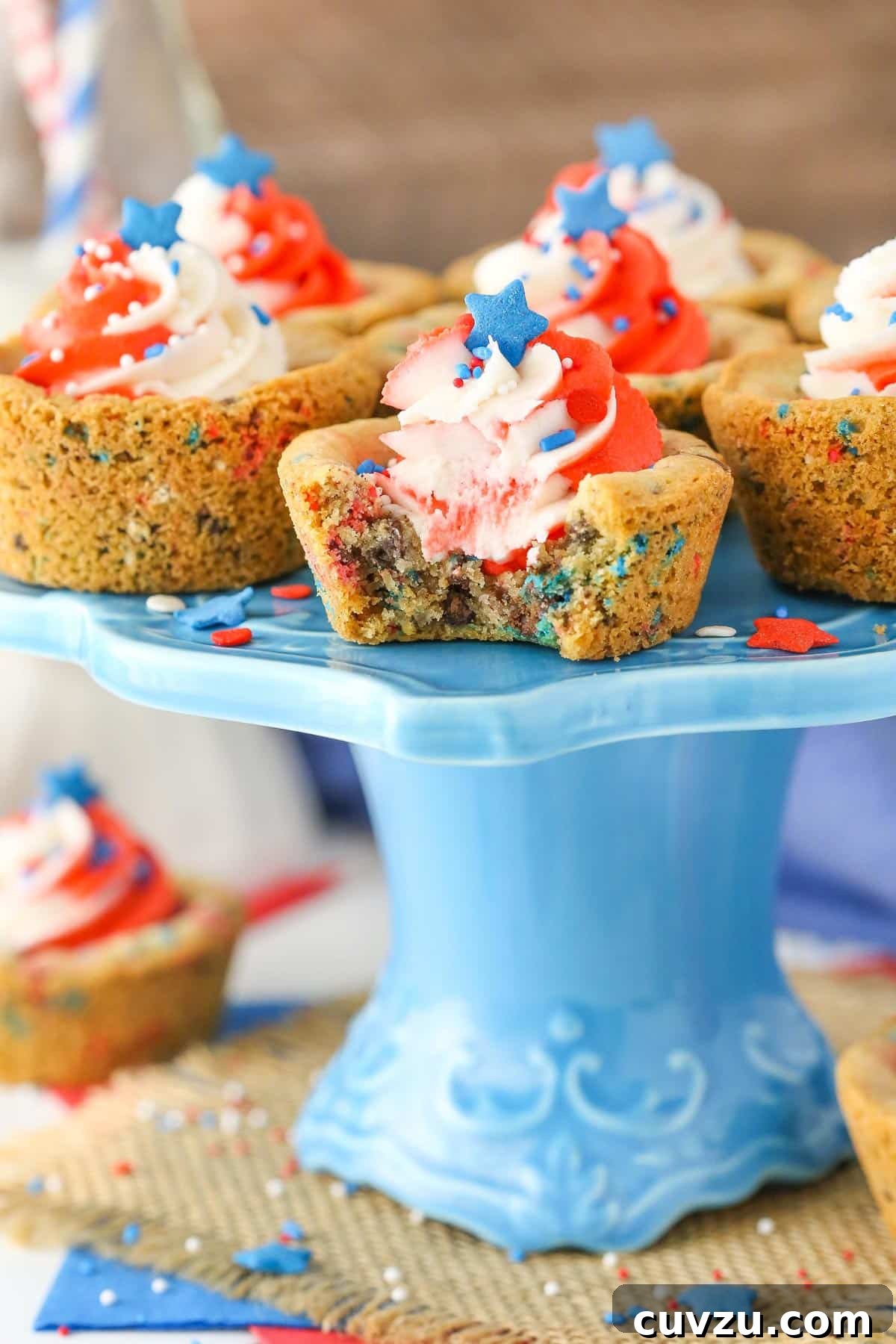Stars and Stripes Chocolate Chip Cookie Cups 7 Several chocolate chip cookie cups on a blue cake stand, with the front cookie cup having a bite taken out, revealing its delicious interior.