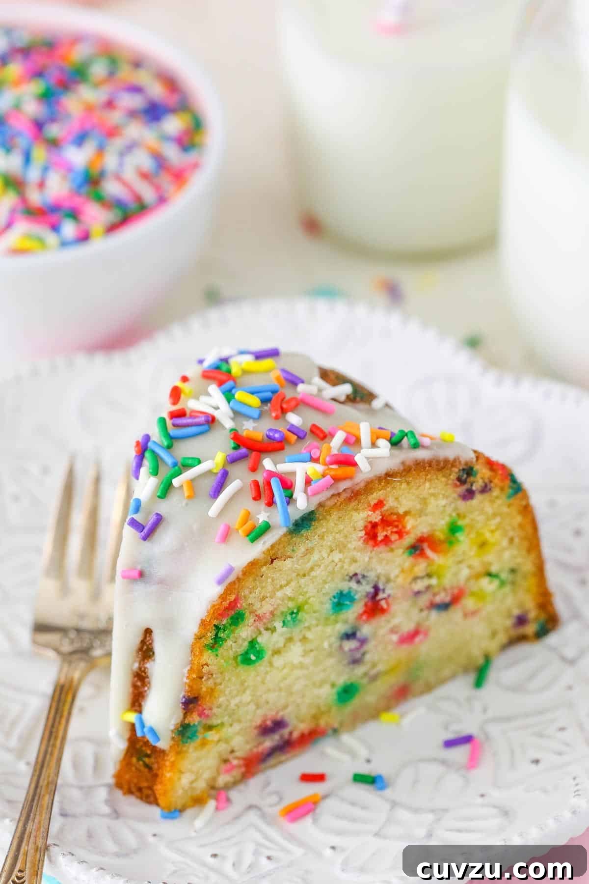 Confetti Joy Bundt Cake 4 A close-up of a slice of funfetti bundt cake on a white plate, emphasizing the dense, moist texture and sprinkle distribution.