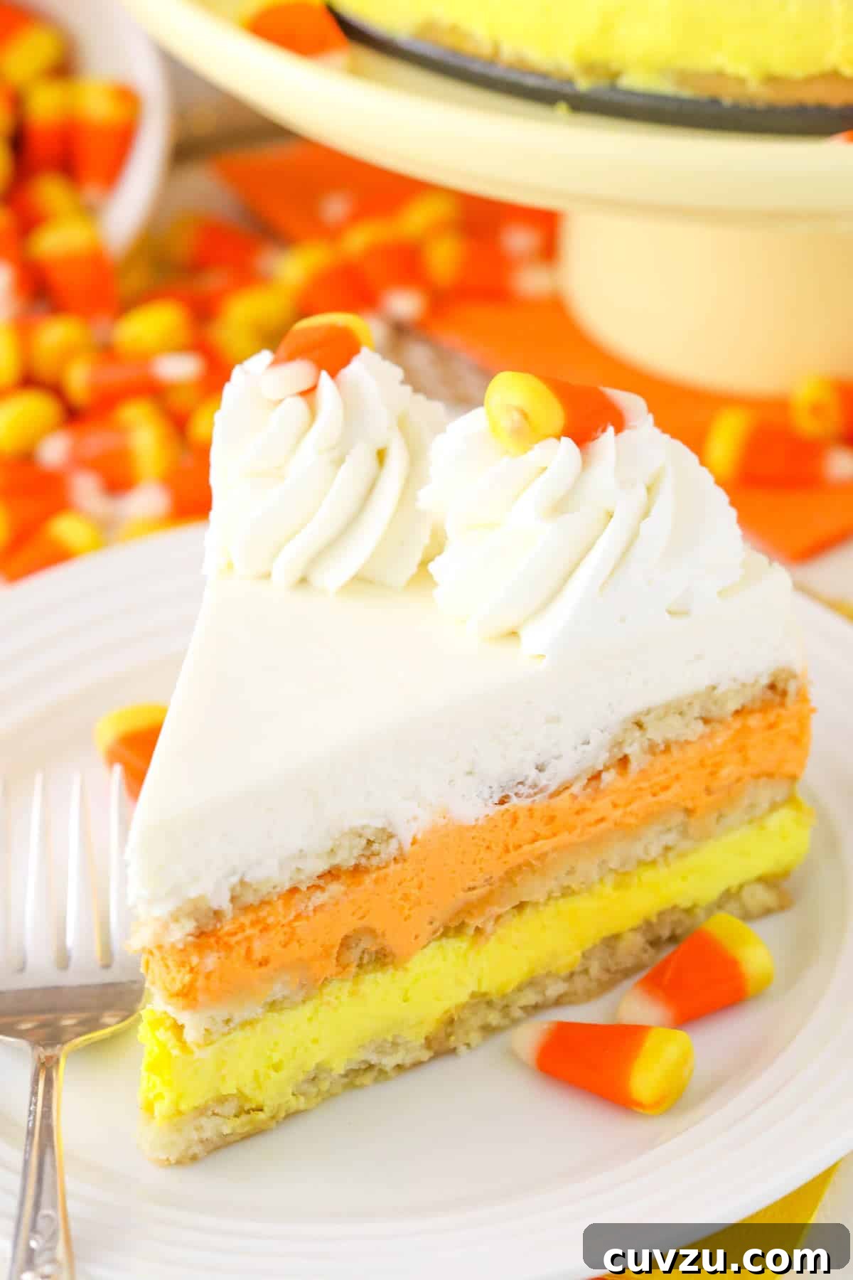 No-Bake Candy Corn Dream 2 A perfectly sliced piece of Candy Corn Icebox Cake, showing its distinct yellow, orange, and white layers, resting on a small white plate.