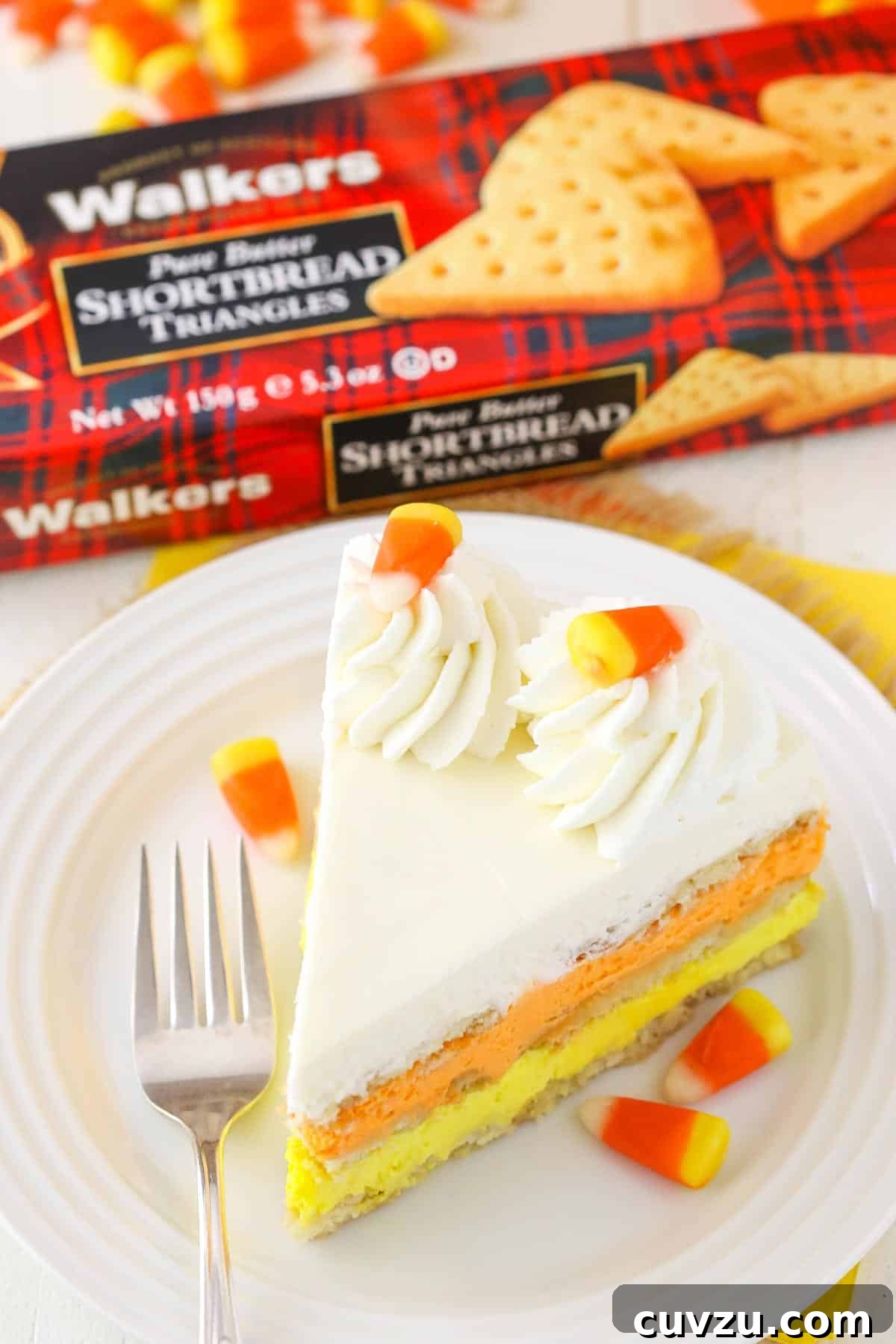 No-Bake Candy Corn Dream 4 A slice of Candy Corn Icebox Cake on a plate, with a box of Walkers Shortbread cookies in the background, highlighting the key ingredient.