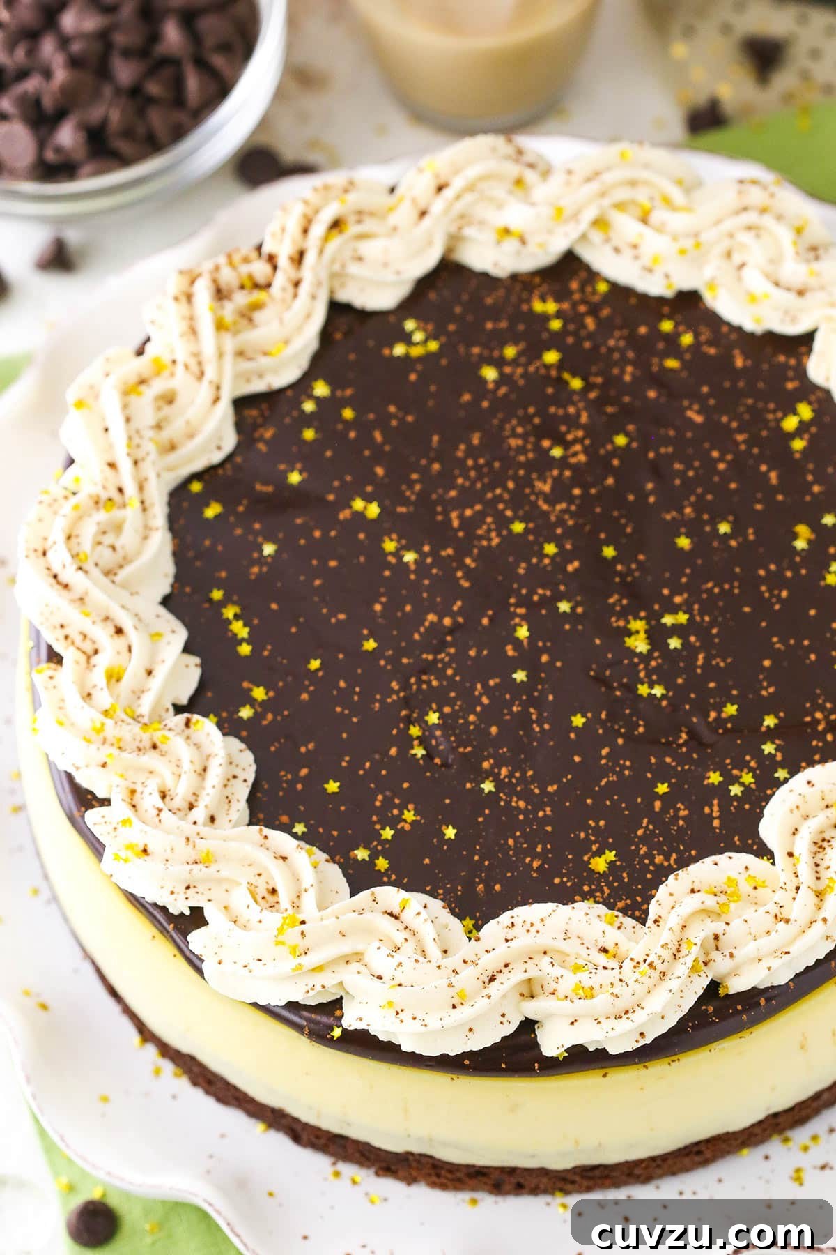 Whole Baileys Brownie Cheesecake: A magnificent dessert. An overhead view of a complete Baileys Brownie Cheesecake on a pristine white platter, adorned with chocolate ganache and elegant whipped cream swirls, ready to be served.