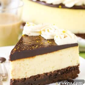 A slice of Baileys Brownie Cheesecake next to a fork on a white plate, ready to be enjoyed.
