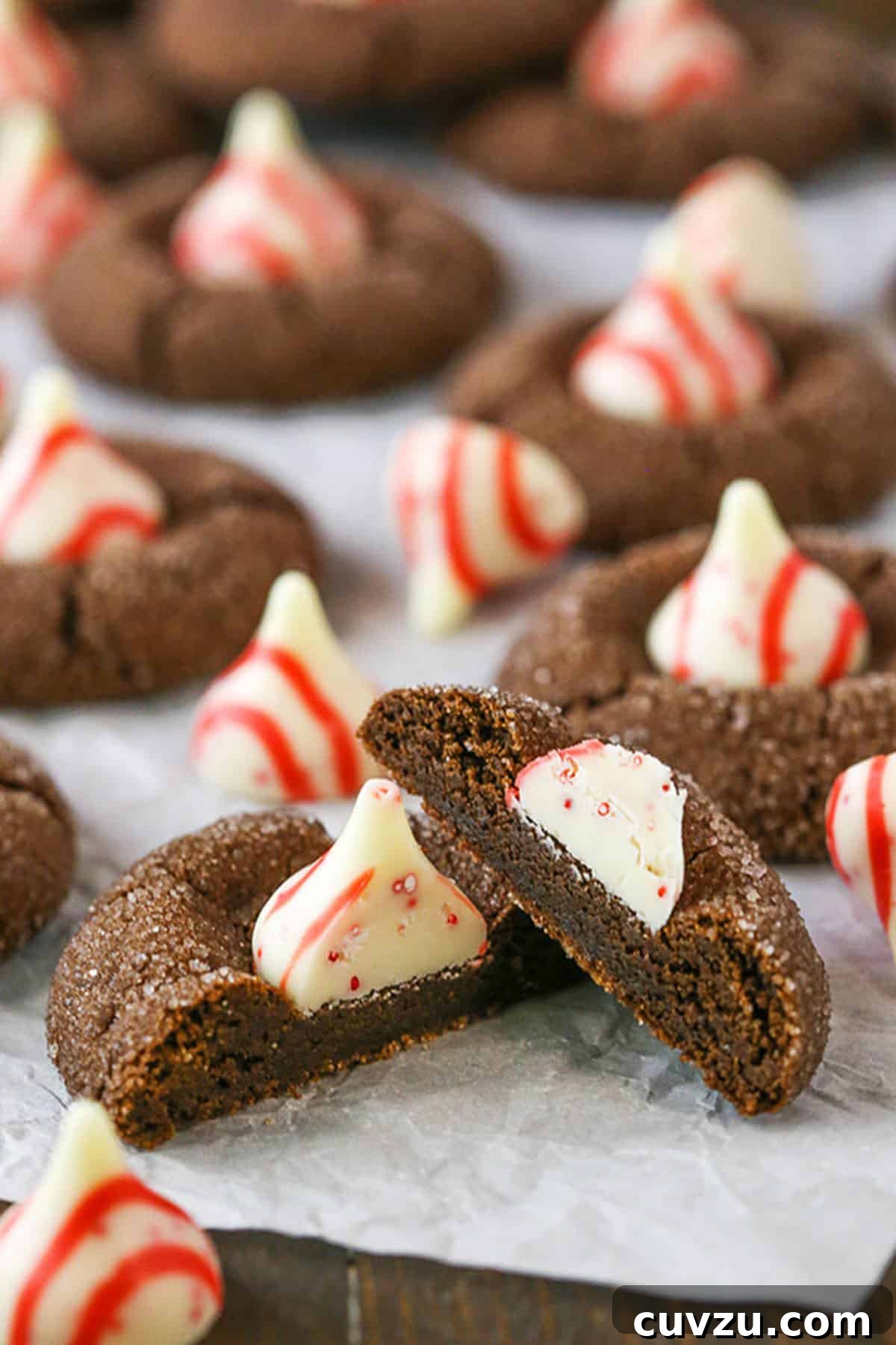 The delightful texture of a Peppermint Chocolate Thumbprint Cookie, perfect for festive indulgence. A Peppermint Chocolate Thumbprint Cookie broken in half, revealing its soft interior, with more whole cookies elegantly arranged in the background.