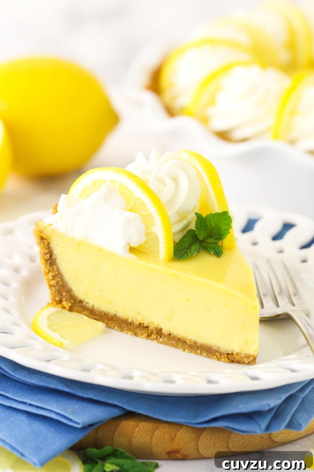 Zesty Lemon Chill Pie 2 A slice of creamy Lemon Icebox Pie on a white plate, garnished with lemon zest and a small metal fork beside it.