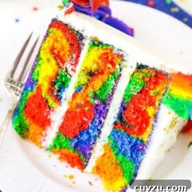 A slice of Rainbow Swirl Cake next to a silver fork on a white plate
