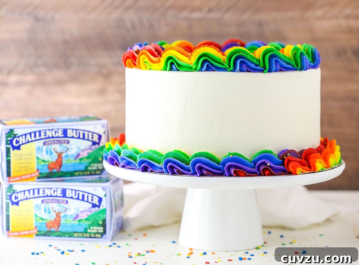 Kaleidoscope Cake 3 A full Rainbow Swirl Cake on a pristine white cake stand, flanked by two boxes of high-quality Challenge Butter, emphasizing premium ingredients.