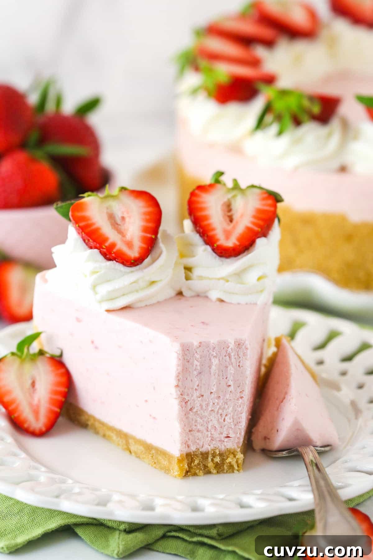 This no-bake strawberry cheesecake is composed of a rich vanilla wafer crust, a luscious strawberry filling, and a light homemade whipped cream, perfect for a refreshing dessert. A close-up of a single slice of no-bake strawberry cheesecake on a plate, with a fork gently taking a bite. The layers of the vanilla wafer crust, the creamy strawberry filling, and the fluffy whipped cream topping are clearly visible, showcasing its inviting texture and deliciousness.