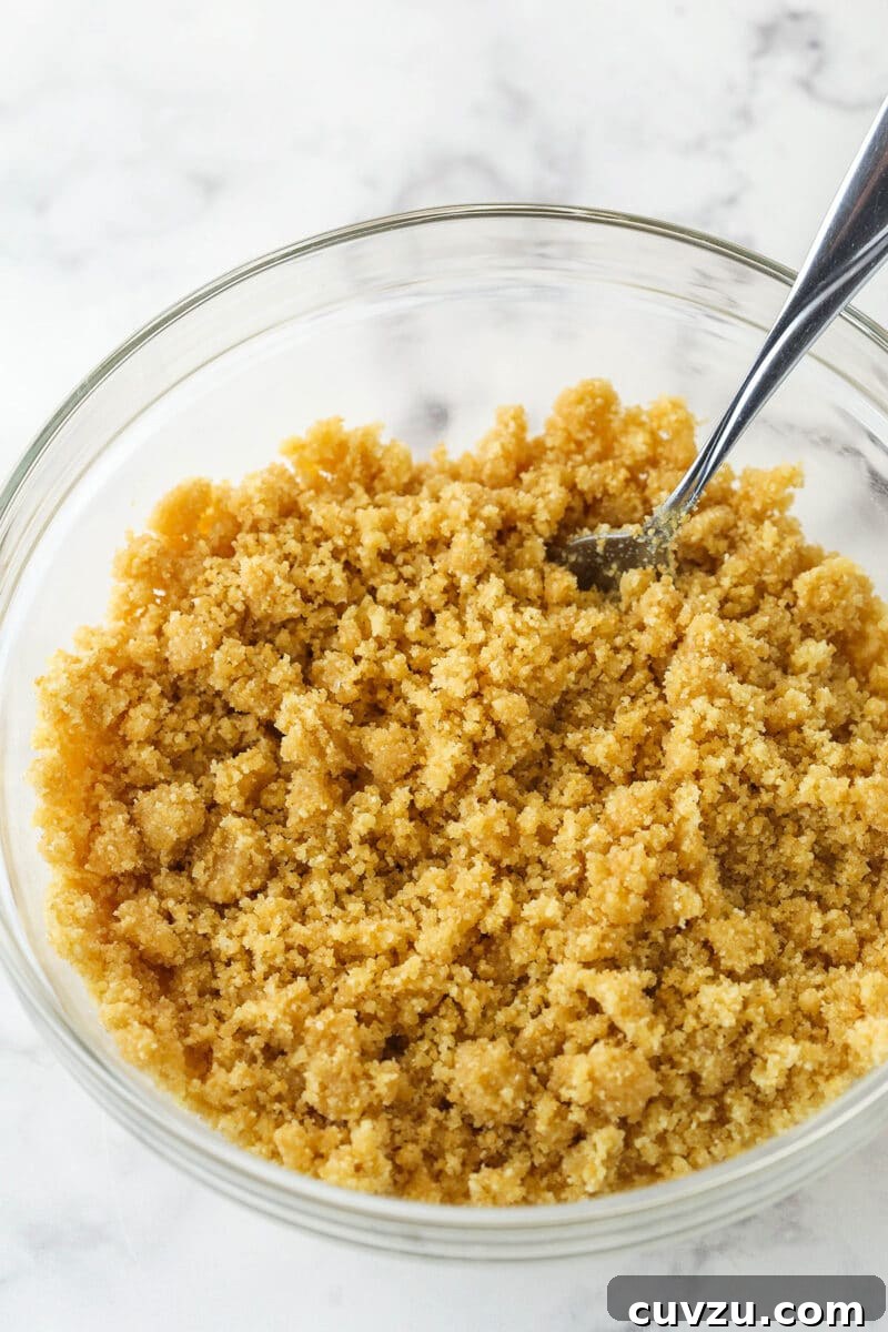 Preparing the buttery vanilla wafer crust for a no-bake strawberry cheesecake, by combining crumbs and melted butter. Mixing together crushed vanilla wafers, sugar, and melted butter in a bowl to form the crust of the no-bake cheesecake, illustrating the initial step of crust preparation.