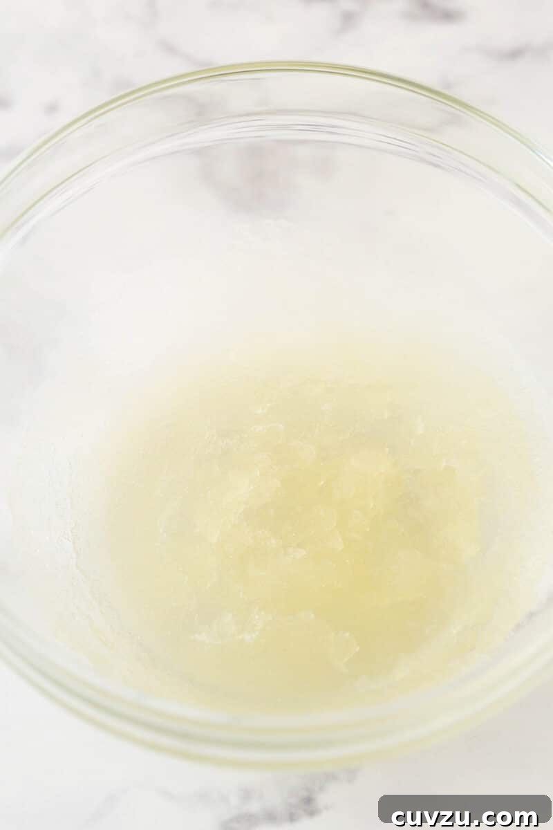 Gelatin and cold water combined in a bowl, blooming for the no-bake strawberry cheesecake filling. Gelatin granules mixed with cold water in a small mixing bowl, showing the essential first step of blooming gelatin for the no-bake cheesecake recipe.