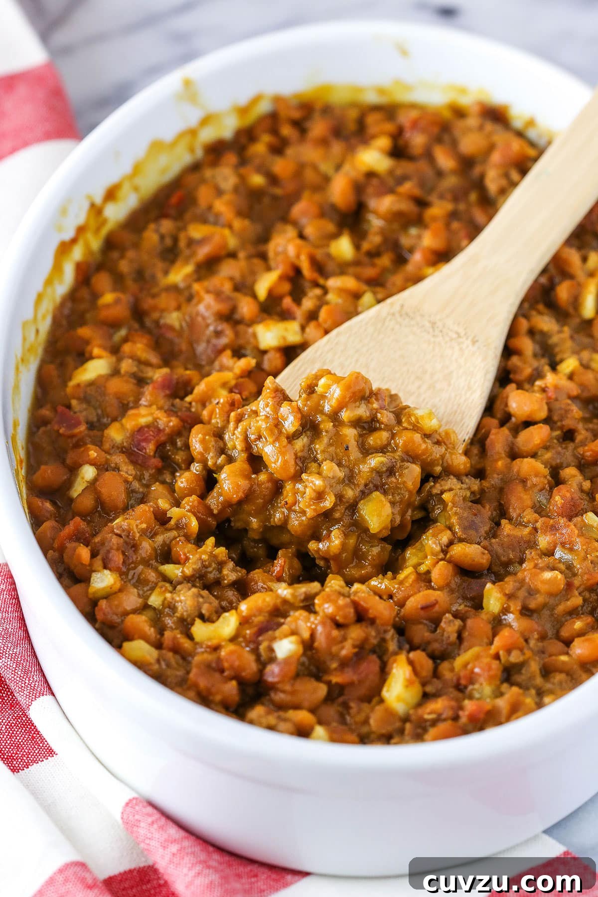 Mom's Legendary Baked Beans 2 A wooden spoon scooping a generous portion of Mom's Amazing Baked Beans from a white serving dish, highlighting their thick and hearty texture.