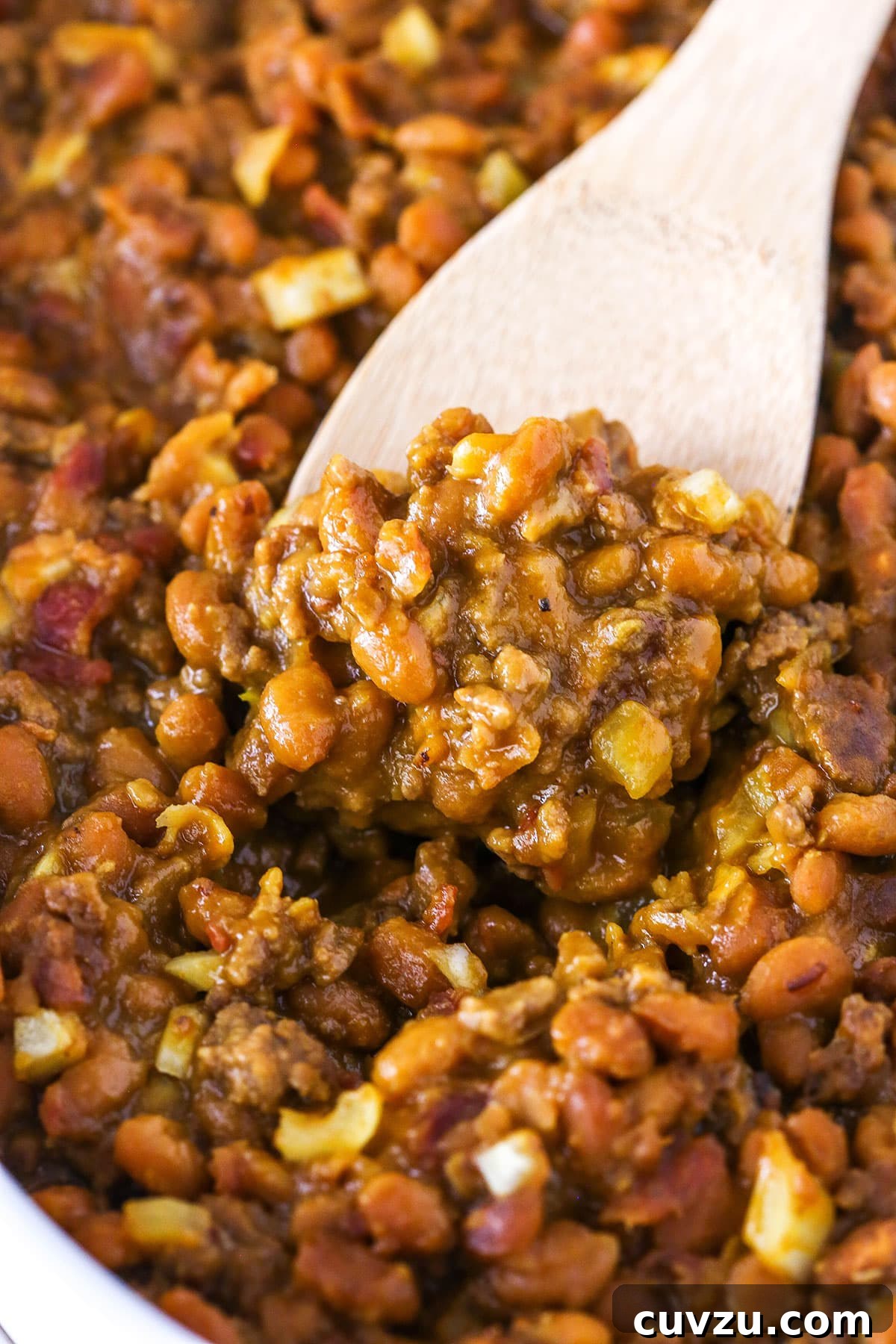 Mom's Legendary Baked Beans 5 A close-up shot of a wooden spoon scooping up a portion of Mom's Amazing Baked Beans, highlighting the chunky texture of the meat and beans.