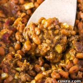 Closeup of scooping up baked beans and beef with a wooden spoon.