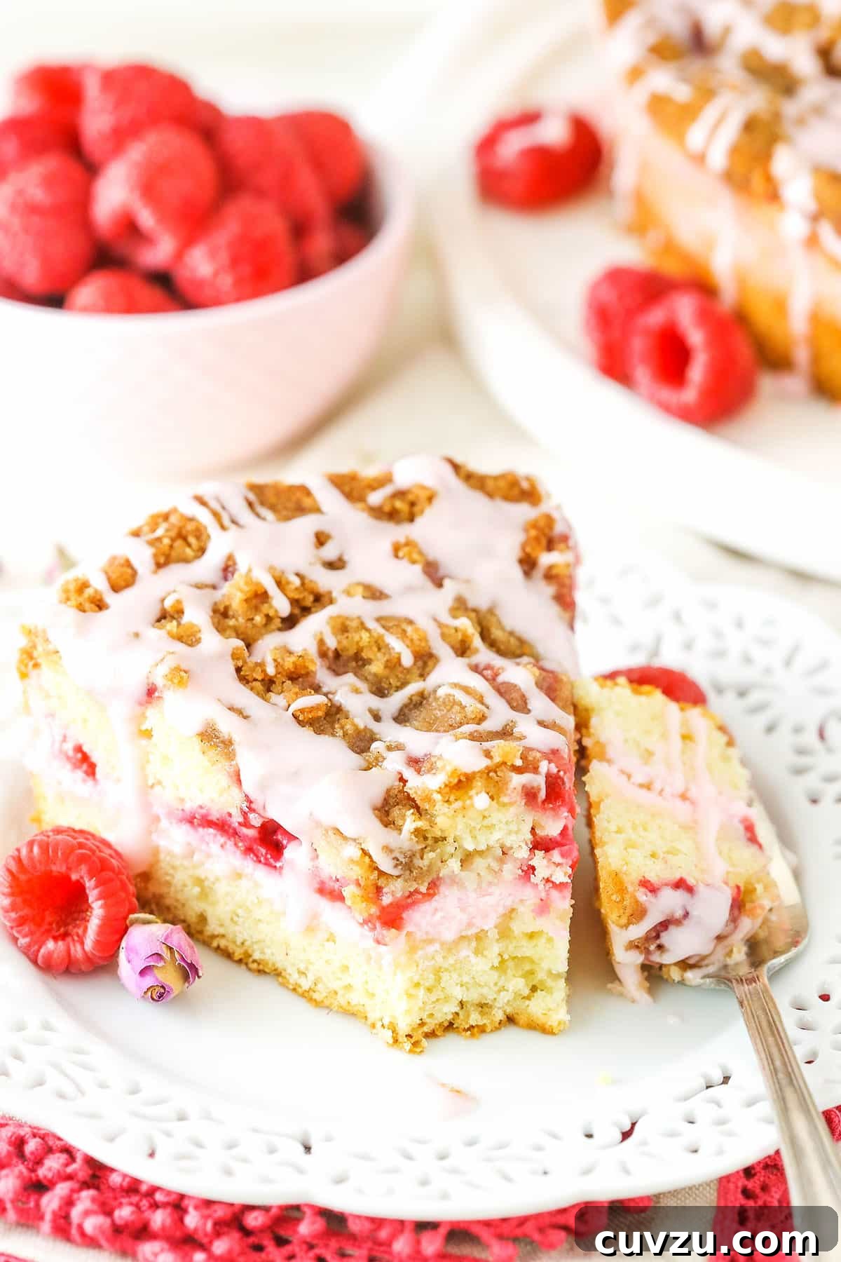 Experience the delightful blend of raspberry and rose in every bite of this incredible coffee cake. A delicious slice of Raspberry Rose Coffee Cake with a bite taken out, perfectly plated beside a fork and garnished with fresh raspberries, inviting you to enjoy its unique flavor.