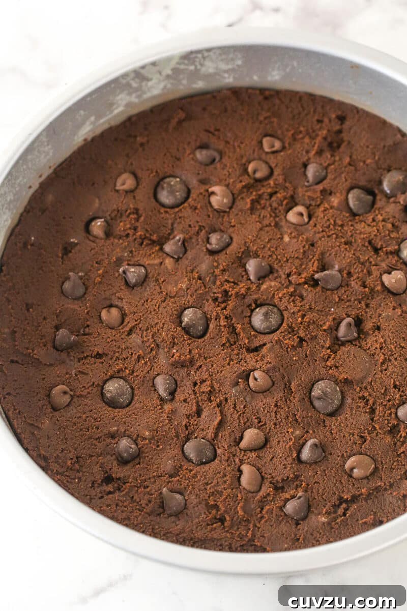 Press the cookie dough into the prepared pan. The unbaked chocolate cookie dough spread evenly into a round cake pan, topped with extra chocolate chips for a beautiful finish.