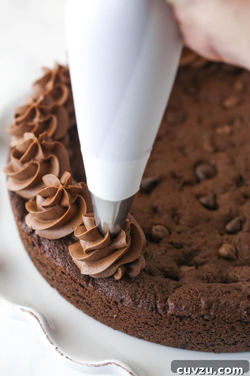 Decorate with decadent chocolate buttercream. A skilled hand piping elegant swirls of rich chocolate buttercream around the perimeter of the cooled triple chocolate cookie cake, adding the final decorative touch.