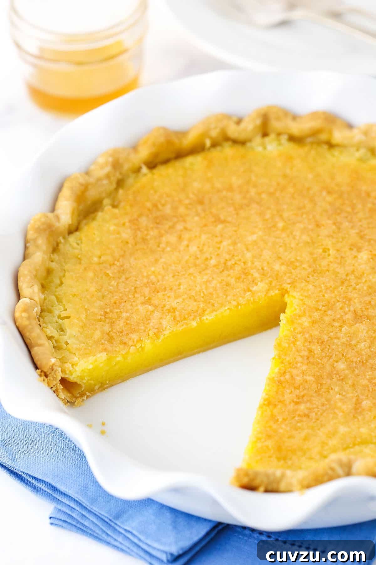 The full Vinegar Pie, showcasing its golden-brown top and inviting texture. Overhead view of a complete Vinegar Pie with one slice removed, presented on a white platter on a blue placemat.