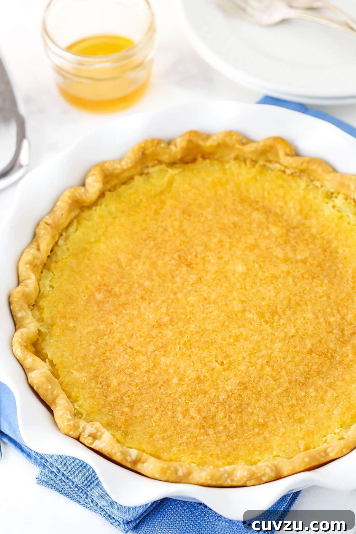 An inviting overhead shot of the whole Vinegar Pie, ready to be sliced. Overhead view of a complete Vinegar Pie in a white platter, resting on a blue placemat.