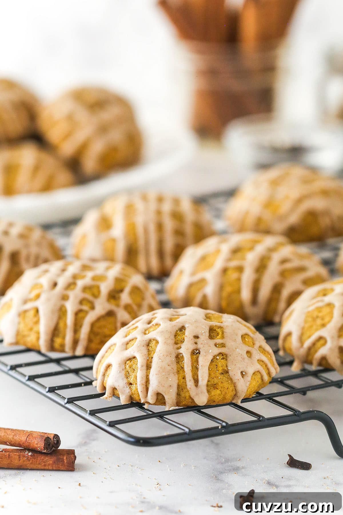 Pillowy Pumpkin Delights 2 Pumpkin cookies with cinnamon glaze on a cooking rack, showcasing their soft texture and sweet topping.