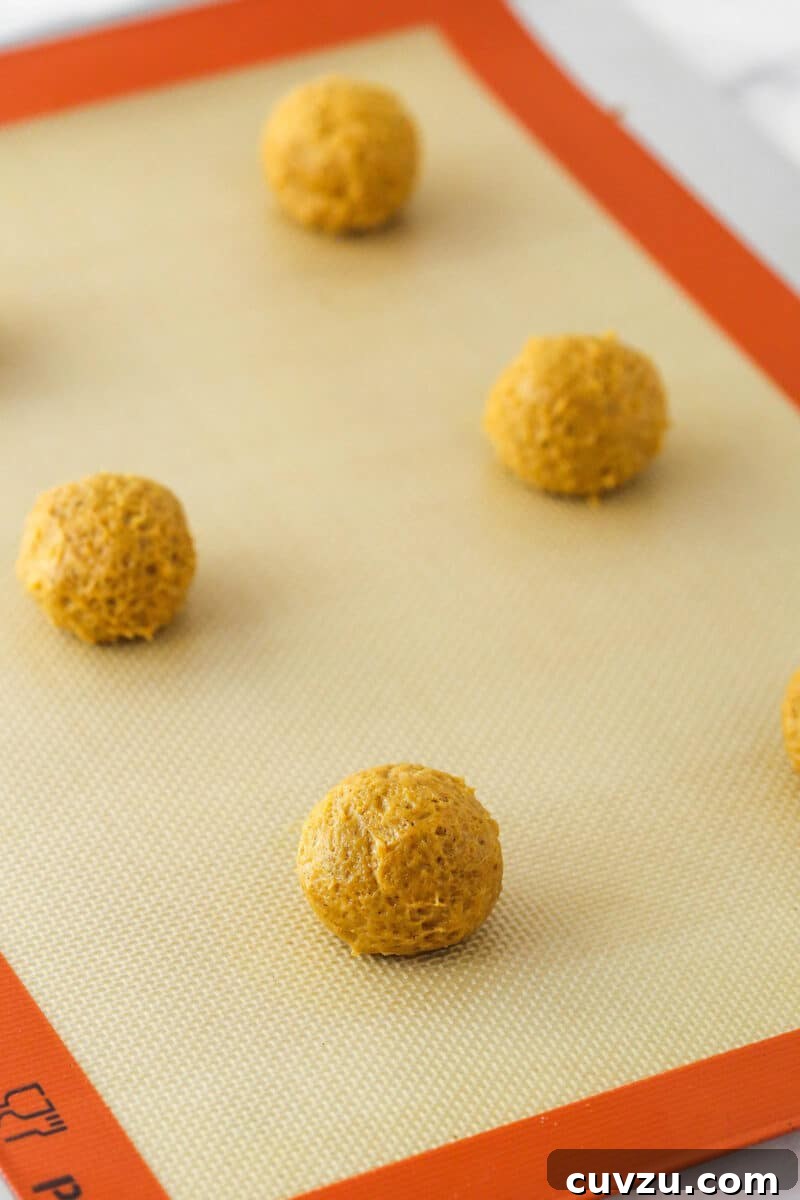 Pillowy Pumpkin Delights 8 Balls of pumpkin cookie dough scooped onto a baking sheet.