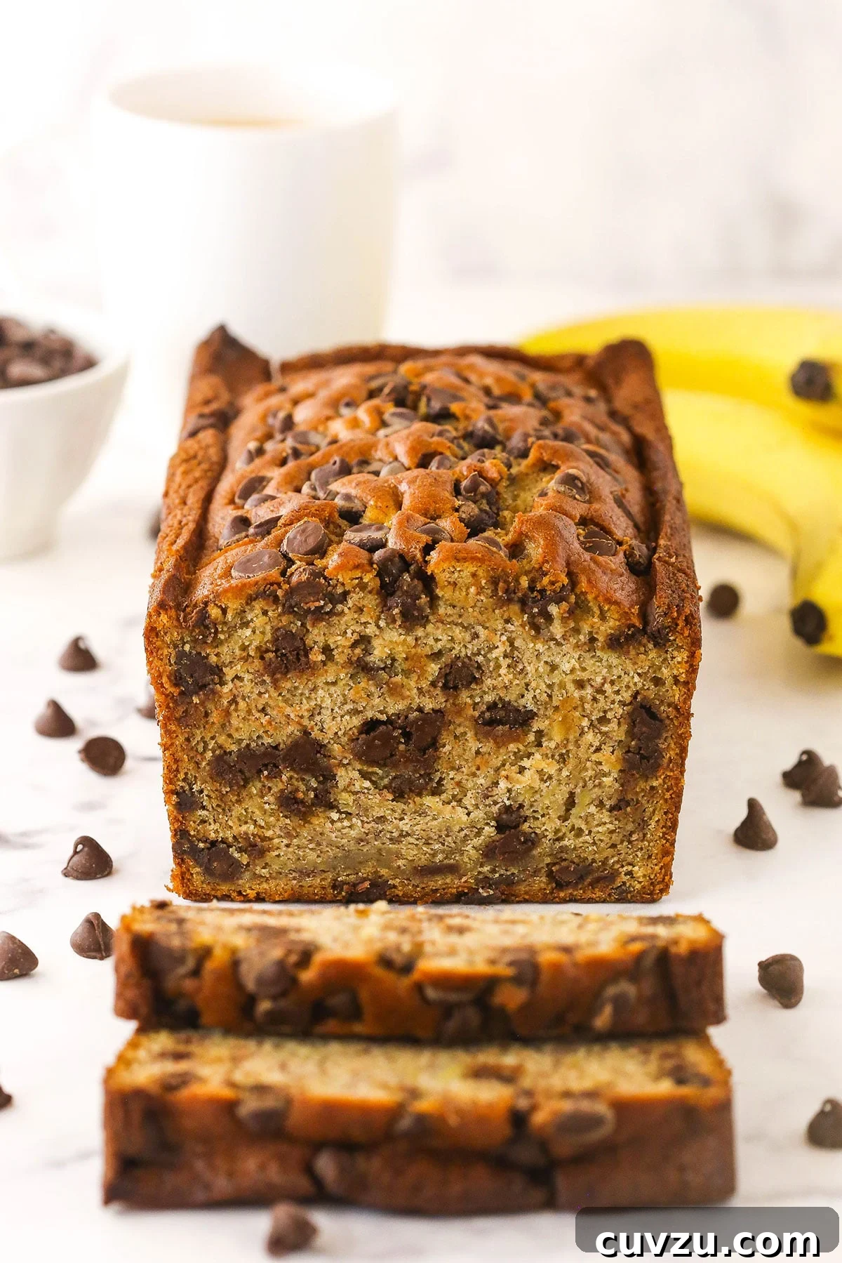This easy Chocolate Chip Banana Bread has the moistest crumb & the softest, fluffiest texture. You'll never follow a different recipe again! A loaf of banana bread with two freshly cut slices in front of it