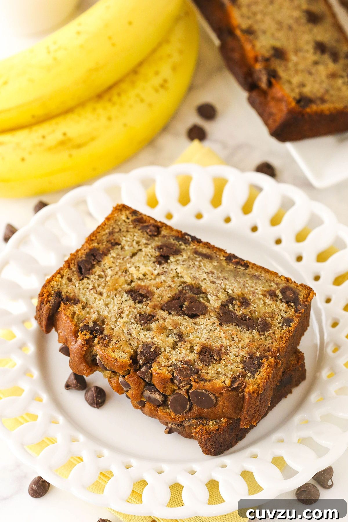 This easy Chocolate Chip Banana Bread has the moistest crumb & the softest, fluffiest texture. You'll never follow a different recipe again! Two pieces of homemade banana bread on a plate on top of a marble kitchen counter