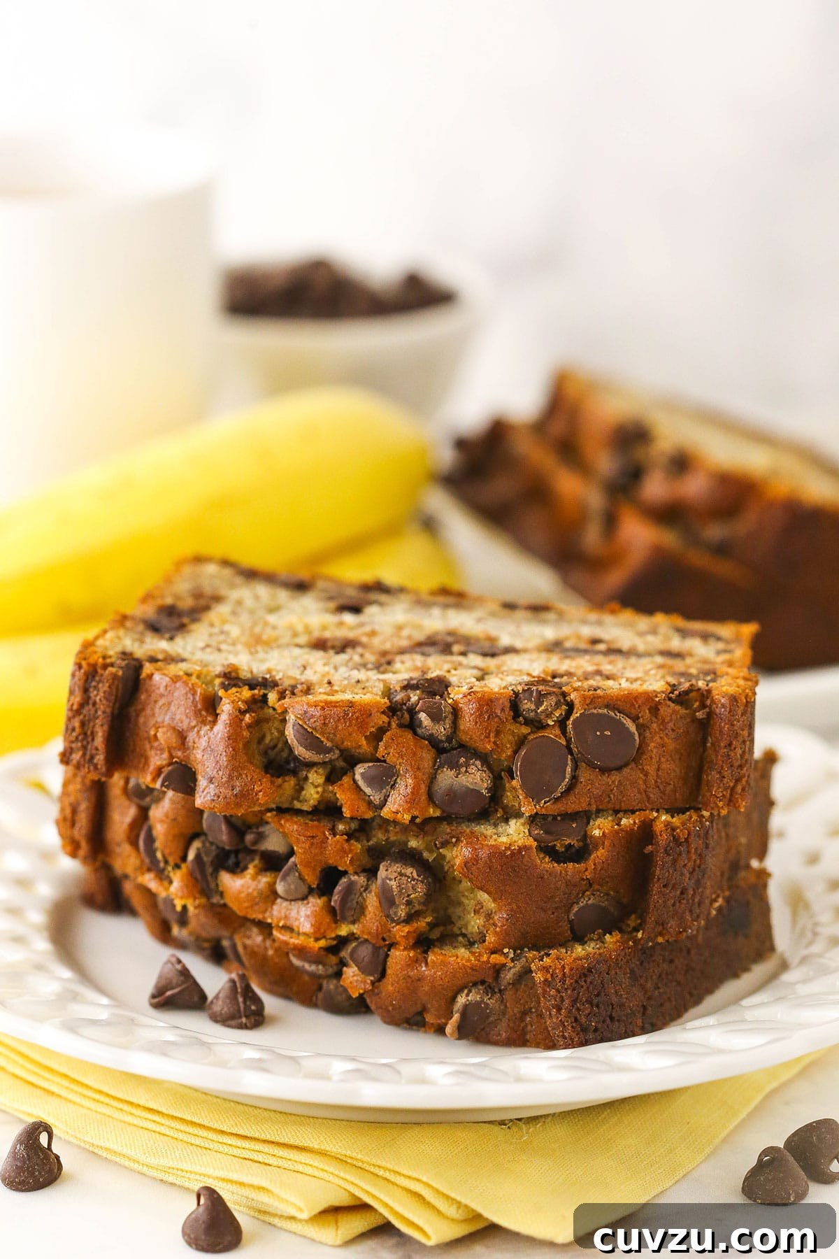 This easy Chocolate Chip Banana Bread has the moistest crumb & the softest, fluffiest texture. You'll never follow a different recipe again! Three slices of banana bread with chocolate chips stacked on top of each other with more bread behind them