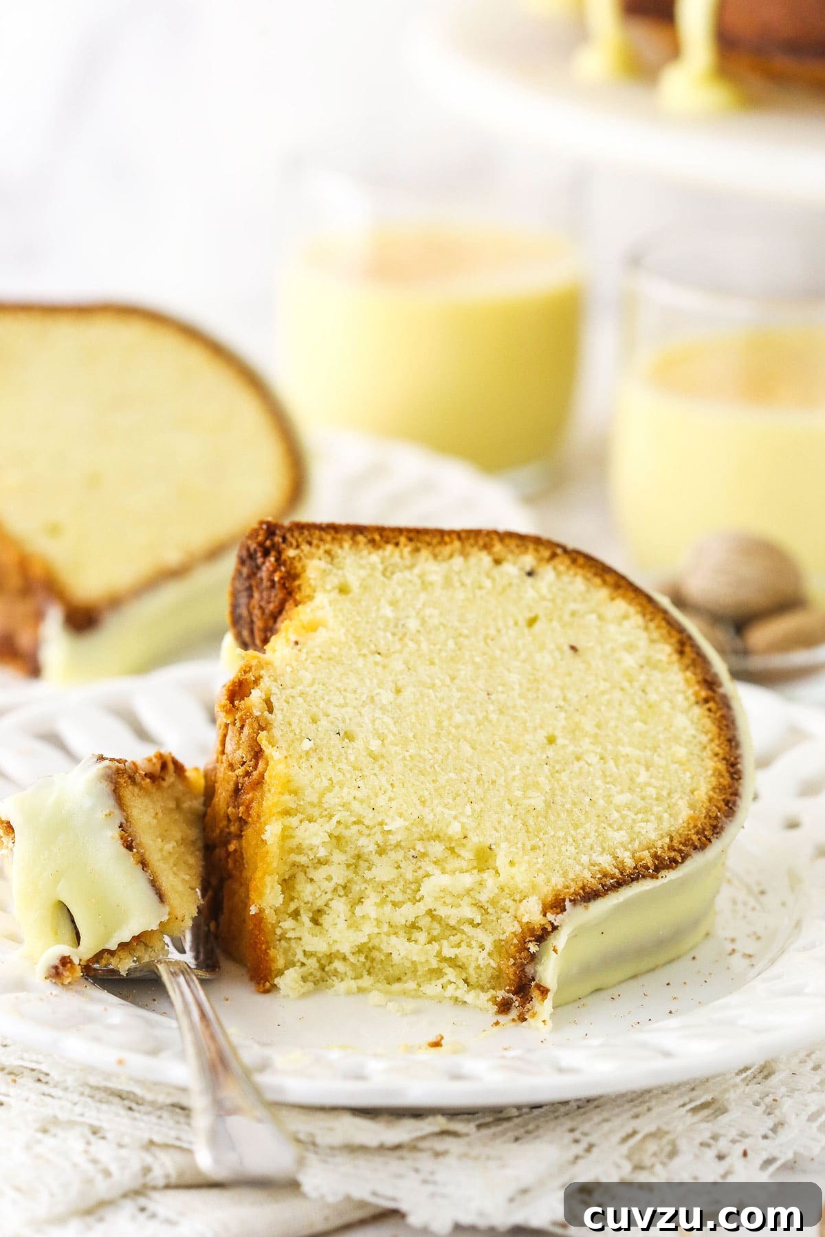 Velvet Eggnog Pound Cake 3 A perfectly sliced piece of eggnog pound cake on a white plate, with a fork ready to take a bite, highlighting its moist texture and golden crust.