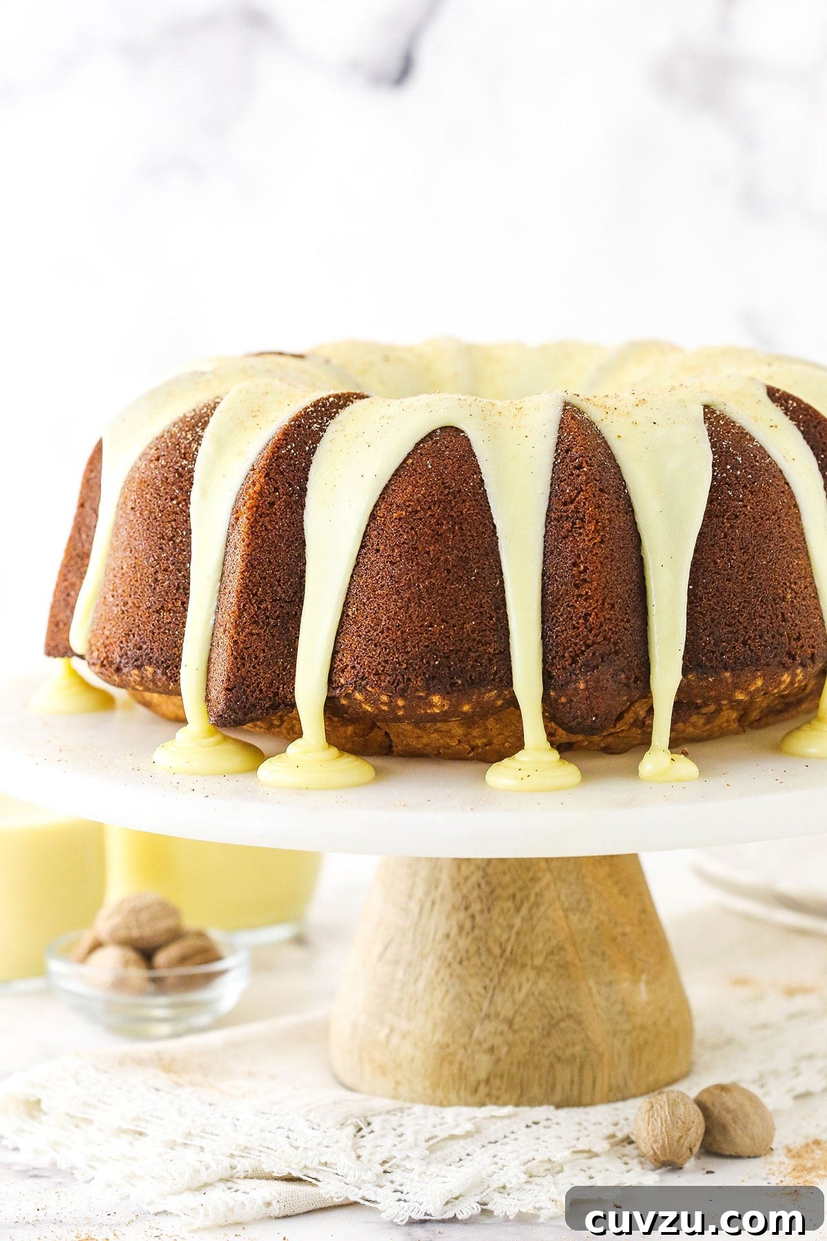 Velvet Eggnog Pound Cake 5 A freshly glazed eggnog bundt cake sitting on a cake stand, with a rich, glossy icing dripping down its sides, set against a granite countertop.
