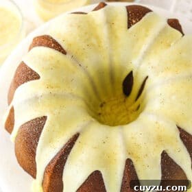 An iced eggnog pound cake on a cake stand with two glasses of eggnog in the background
