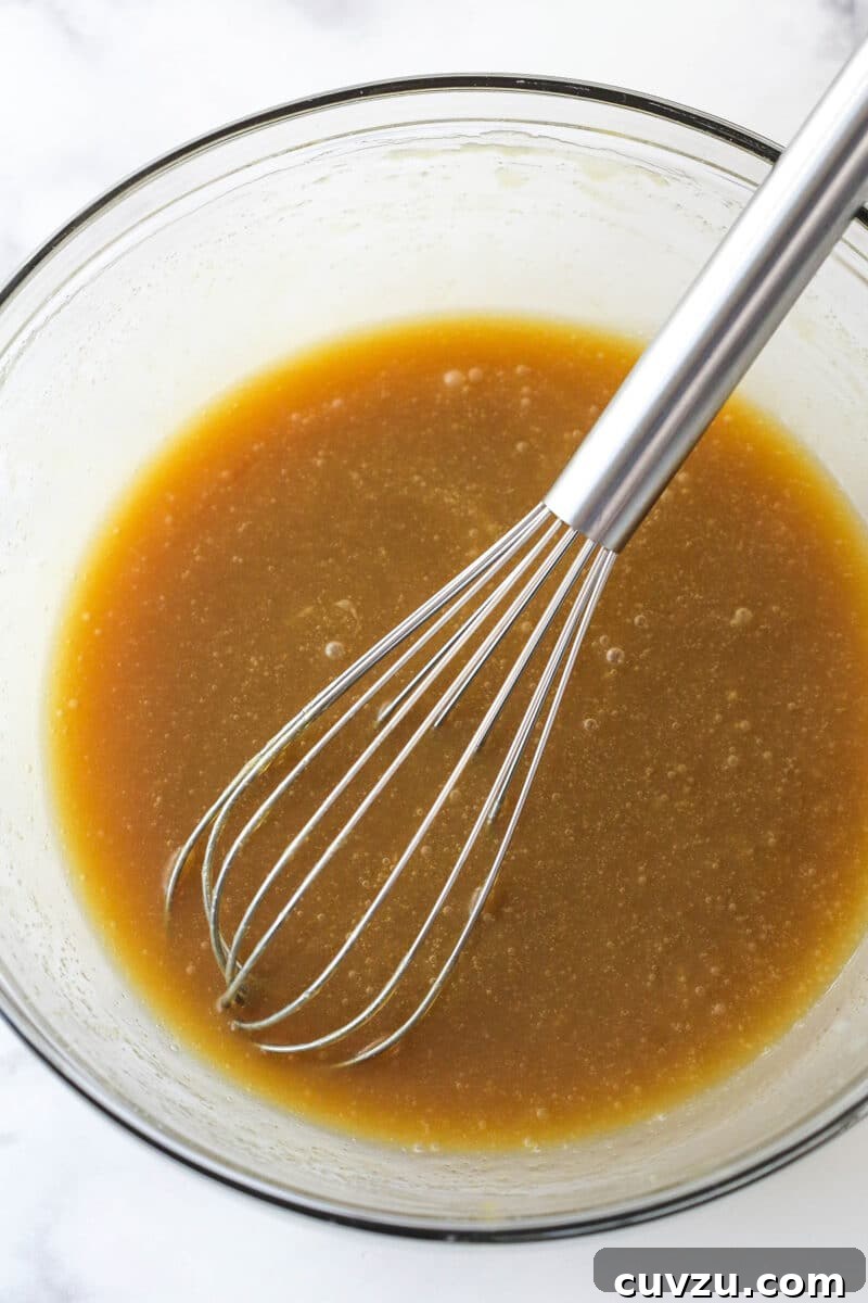 Decadent Caramel Apple Blondie Cheesecake 5 A mixture of melted butter and light brown sugar being whisked in a glass mixing bowl.