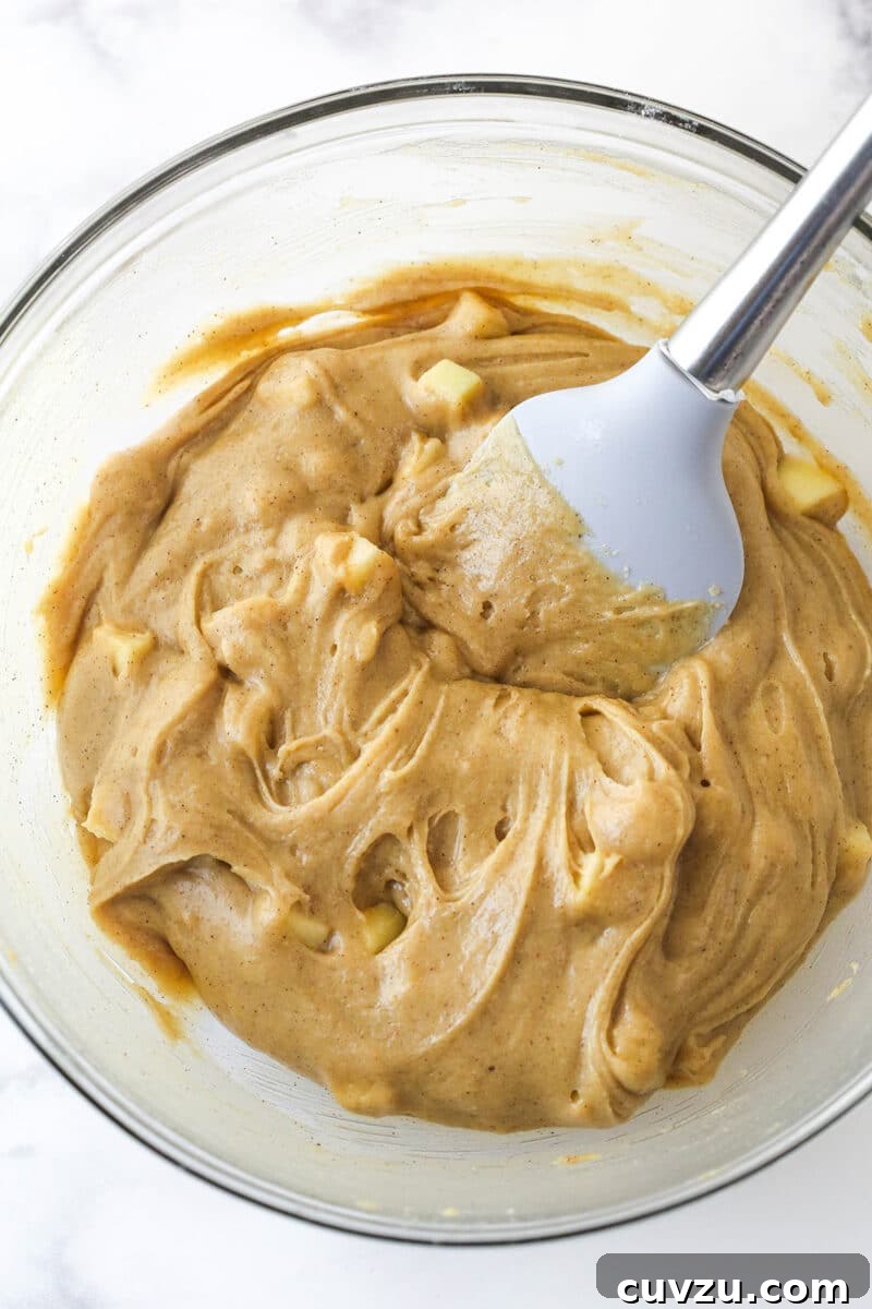 Decadent Caramel Apple Blondie Cheesecake 6 A glass mixing bowl filled with rich blondie batter, showing visible pieces of apple mixed in.