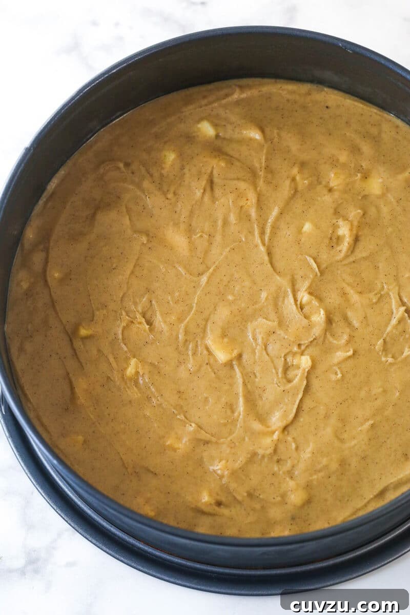 Decadent Caramel Apple Blondie Cheesecake 7 Apple blondie batter evenly spread into the bottom of a parchment-lined springform pan, ready for baking.