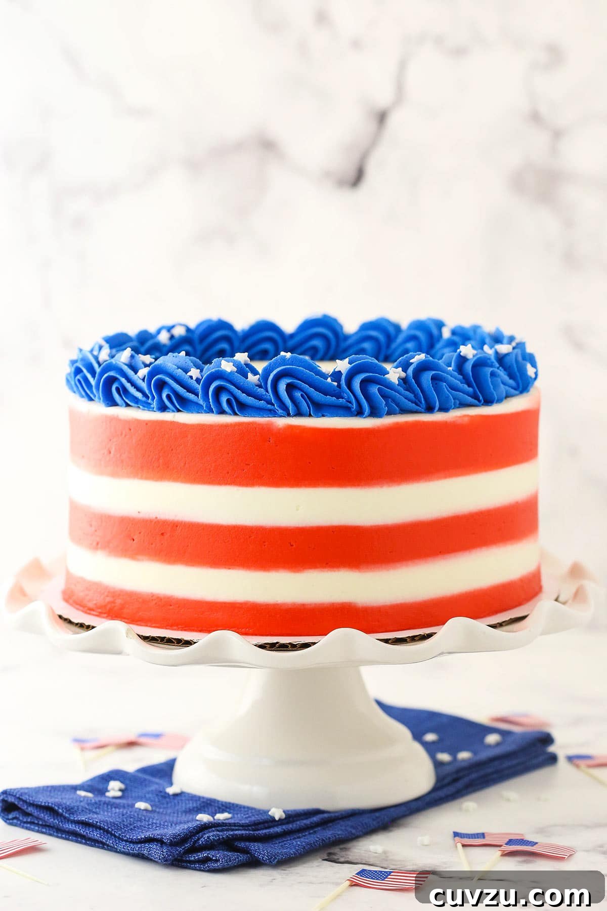 Fourth of July Swirl Cake 7 A tall cake stand holding a 4th of July marble cake with small American flag toothpicks on the counter beneath it