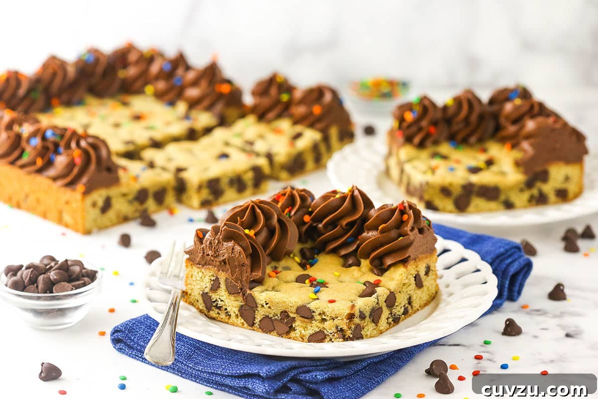 This easy Sheet Pan Cookie Cake features loads of chocolate chips and a rim of creamy chocolate frosting. It's perfect for feeding a crowd! A piece of chocolate chip cookie cake on a plate with more pieces in the background