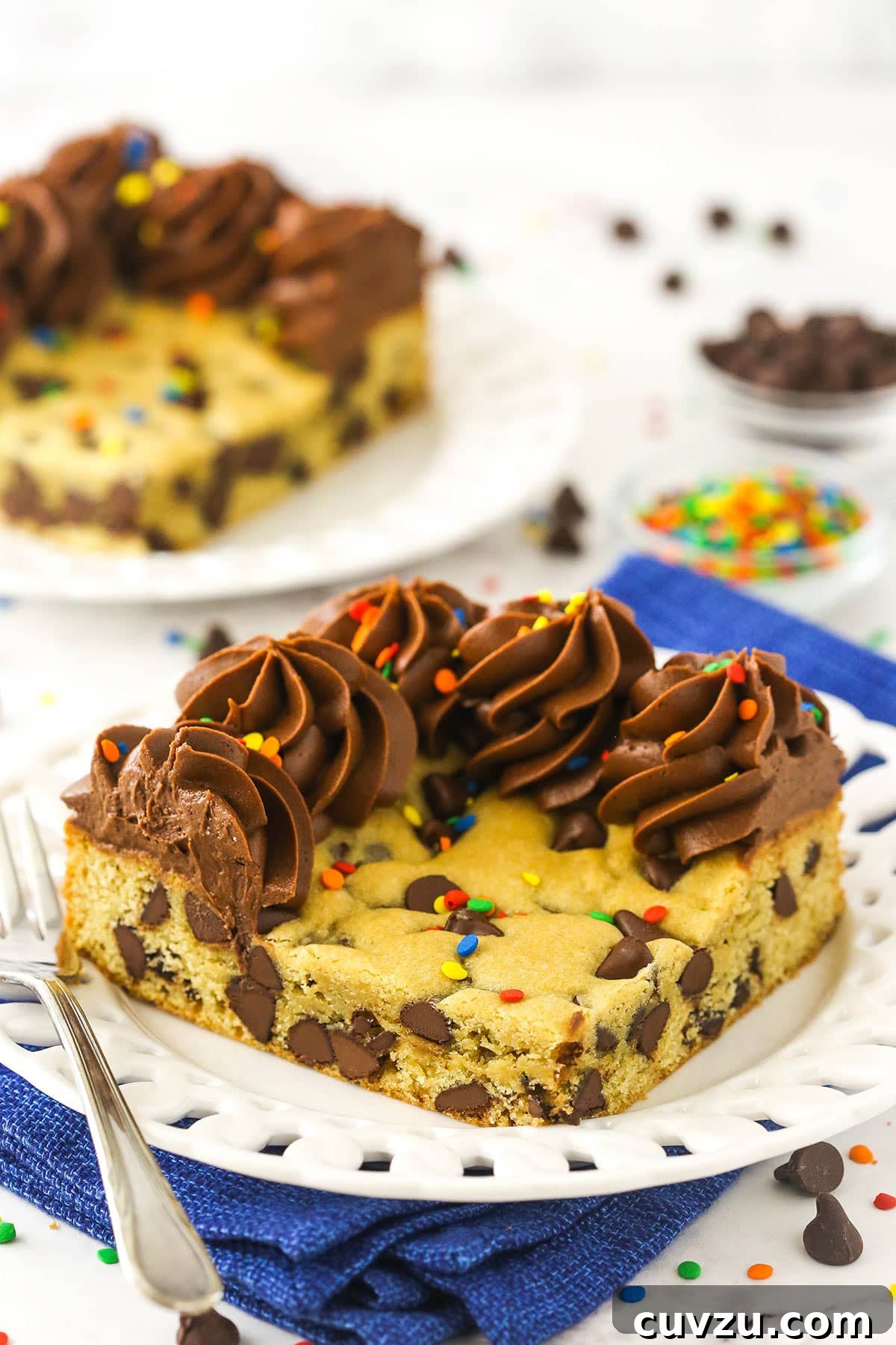 This easy Sheet Pan Cookie Cake features loads of chocolate chips and a rim of creamy chocolate frosting. It's perfect for feeding a crowd! A white dessert plate holding a big slice of chocolate chip cookie cake