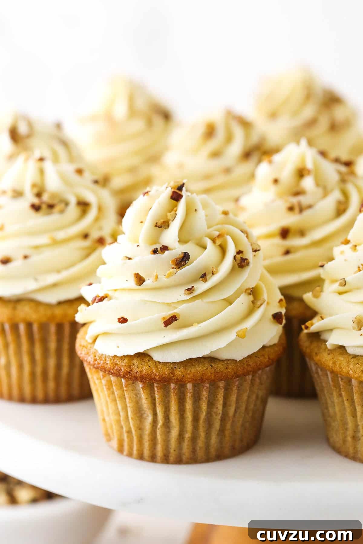Soft brown sugar cupcakes are stuffed with gooey pecan pie filling & topped with creamy pecan pie frosting in this decadent homemade dessert. A batch of exquisitely frosted Pecan Pie Cupcakes, garnished with finely chopped toasted pecans, arranged on a beautiful cake stand.
