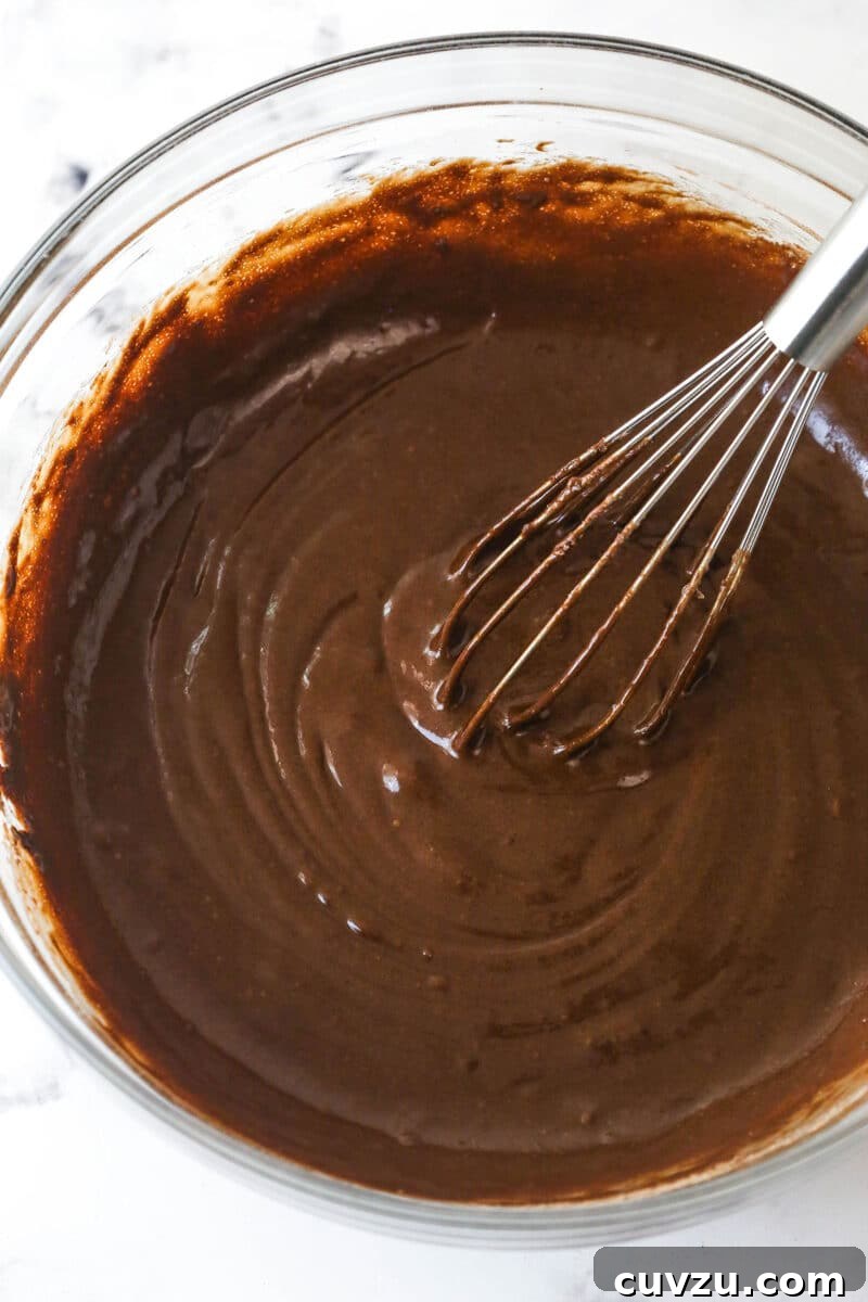 These Black Bottom Cupcakes combine two desserts in one with a rich chocolate cupcake and a creamy chocolate chip cheesecake filling. Chocolate cupcake batter in a bowl with a whisk