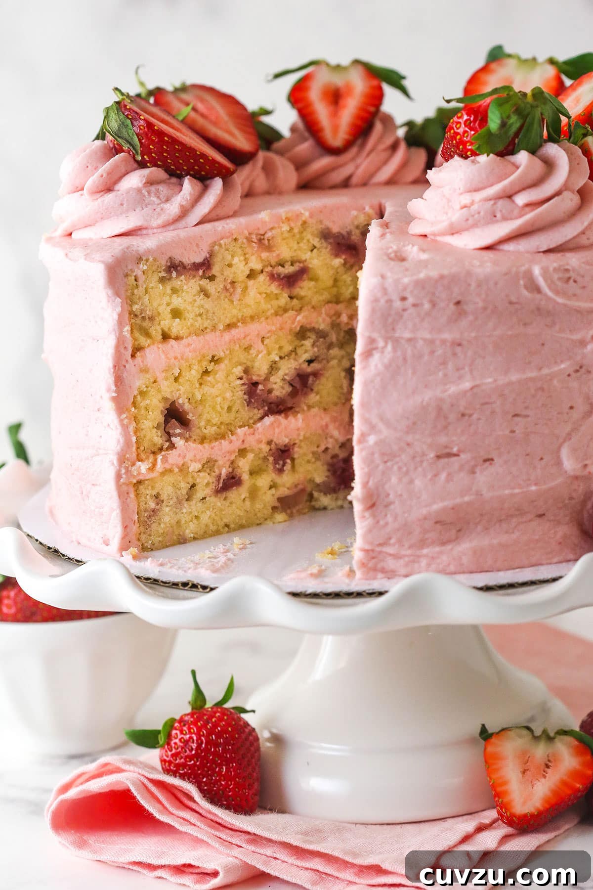 A fresh strawberry cake on a cake stand with a slice missing to show the layers inside