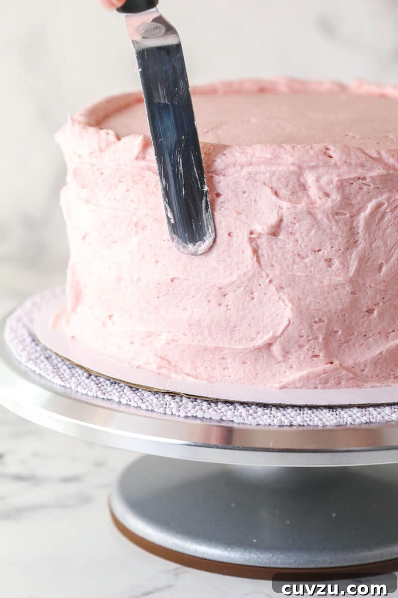 Smoothing strawberry buttercream on the outside of a layer cake